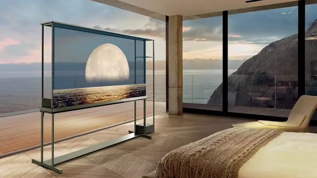 The corner of a bedroom with floor-to-ceiling windows looks out onto a beautiful ocean vista with a transparent TV displaying the moon situated on one side.