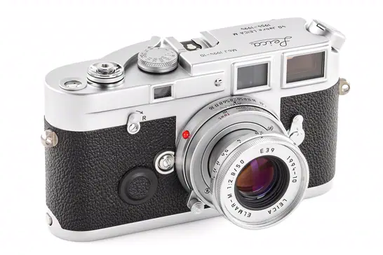 A vintage film camera made from silver metal with a textured black body in an all-whote background.