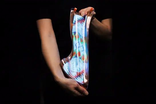 Disembodied hands pull on either end of a slexible screen depicting colorful shapes.