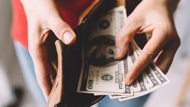 A woman pulls $100 bills out of a wallet.