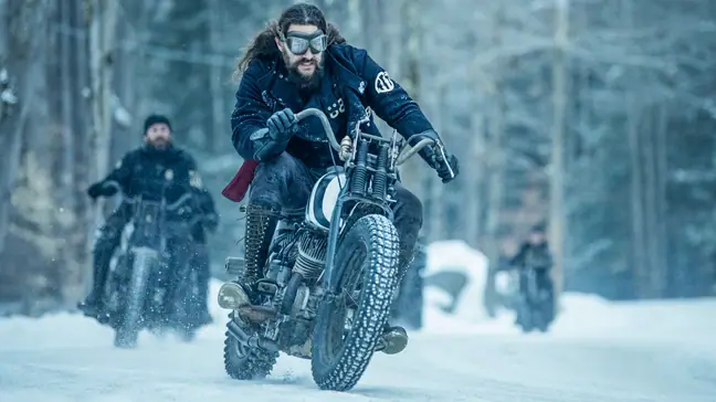 Jason Momoa riding a motorcycle in the snow.